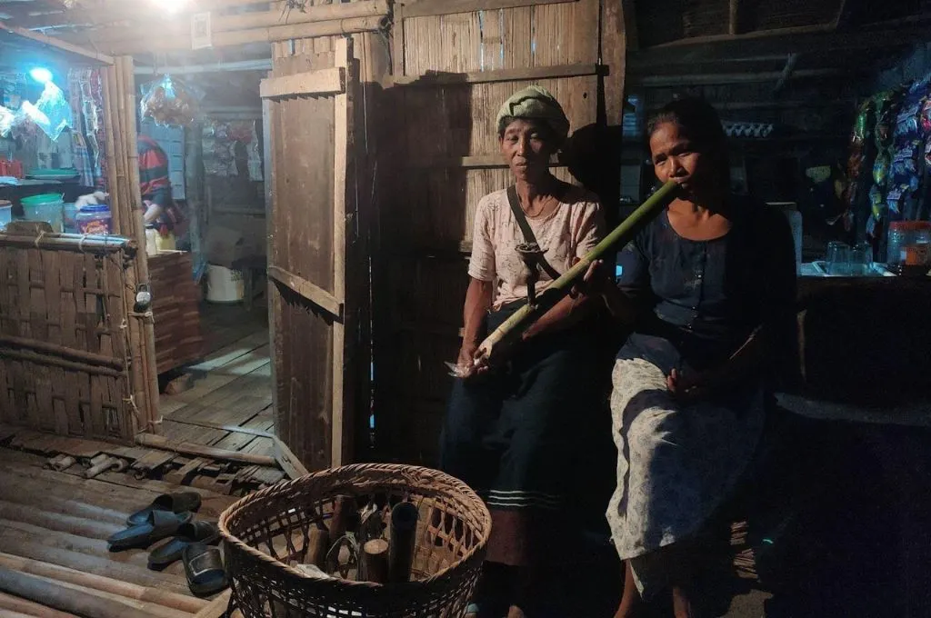 Ranglong women smoking a bamboo hookah at a local shop in Laikhua; a traditional bamboo basket in front of them.--bamboo-based livelihoods