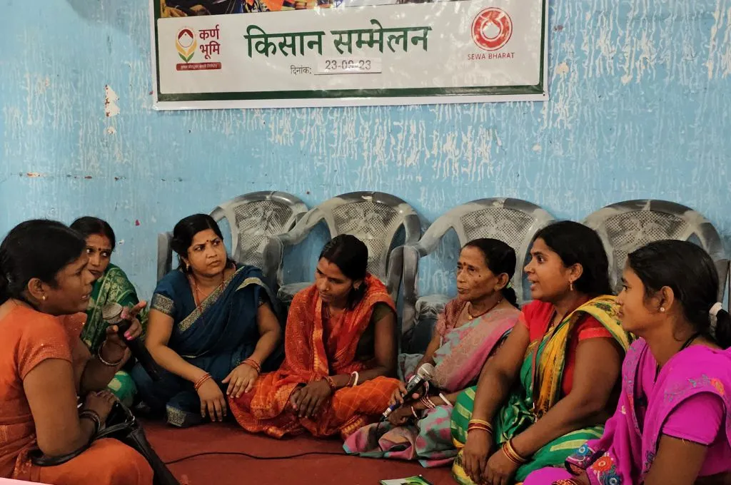 seven women sitting on the floor with a banner saying "kissan sammelan" hung on a wall in the background--Farmer Producer Organisations (FPOs)